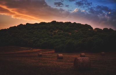 Hay bales on field against sky at sunset