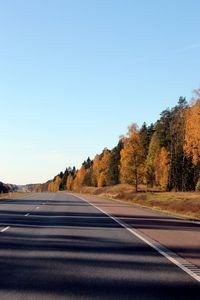 Road amidst trees against clear blue sky