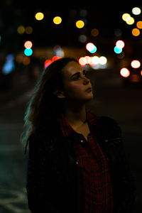 Thoughtful young woman standing against lens flare at night