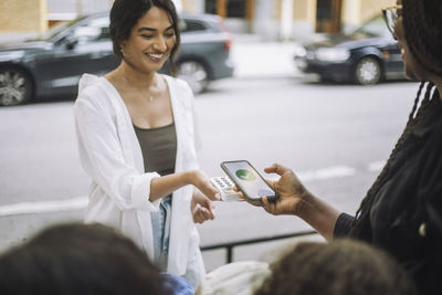 Smiling female vendor taking online payment from customer while selling at market