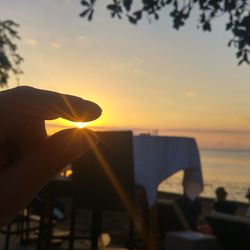 Hand holding sun over sea against sky during sunset