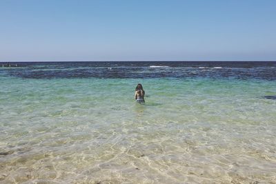 Rear view of woman standing in sea against clear sky