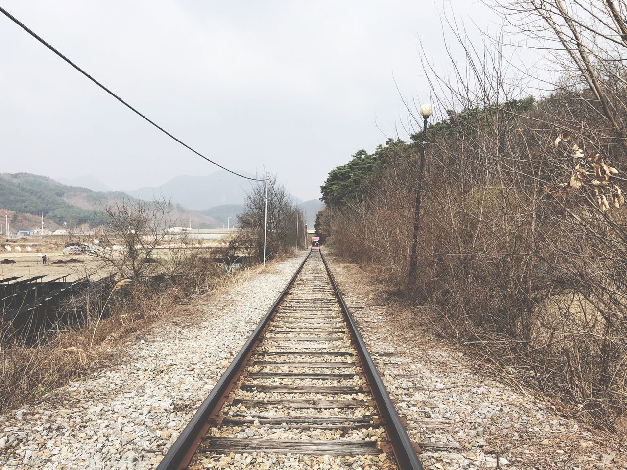 railroad track, track, rail transportation, transportation, sky, direction, the way forward, tree, nature, plant, diminishing perspective, day, no people, vanishing point, mode of transportation, land, outdoors, non-urban scene, mountain, clear sky