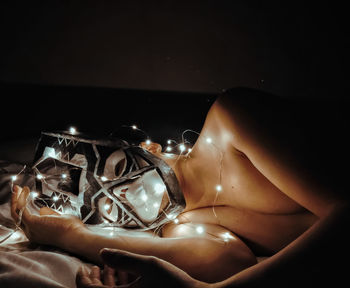 Shirtless young man with string lights wearing mask while lying in darkroom