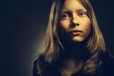 Close-up portrait of serious young woman against black background