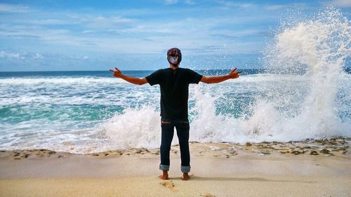 Full length of man with arms outstretched gesturing while standing at beach against sea