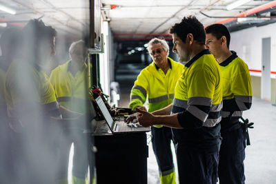 Group of skilled male engineers in uniform using gadgets while examining electrical equipment in modern building