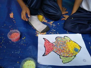 Children making fish with sprinkles on carpet