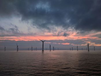 Windmills on sea against cloudy sky during sunset