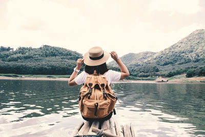 Rear view of woman sitting by lake on wooden raft