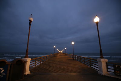 Illuminated pier over sea at night