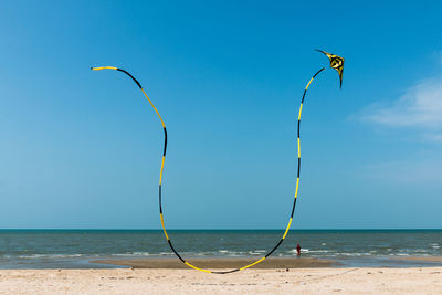 Person flying striped kite at beach against sky