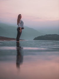 Woman standing in sea against sky during sunset