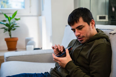 Male with eyesight disability scrolling mobile phone while sitting on couch at home