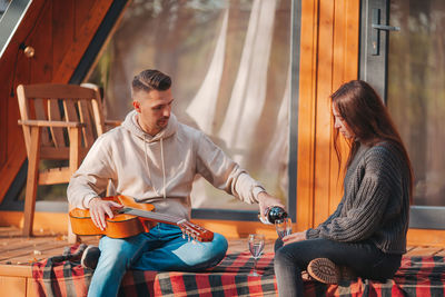 Man pouring wine in glass while sitting with woman outdoors