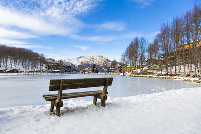 Benches on snow covered bench against sky