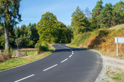 Country road amidst trees against sky