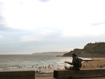 Man sitting on beach against sky