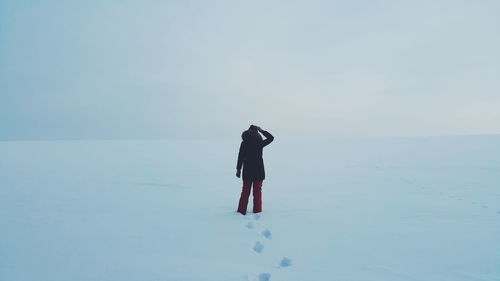 Rear view of person standing on snow covered field against sky