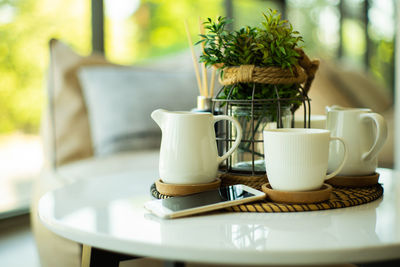 Closeup set of white ceramic cup and jug of tea and coffee with mobile phone.