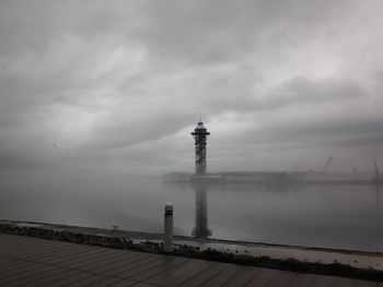 Lighthouse by sea against cloudy sky