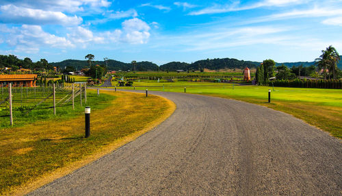 Empty road leading towards grassy field against cloudy sky