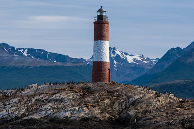 Lighthouse by mountain against sky