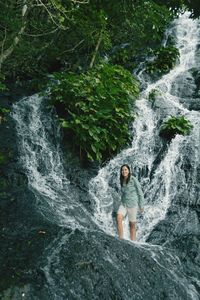 Woman standing against waterfall in forest