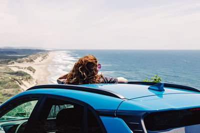 Woman looking on the beautiful overlook of the pacific ocean through the sunroof of her car. 