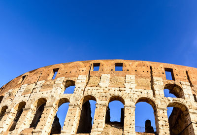 Low angle view of coliseum against clear blue sky