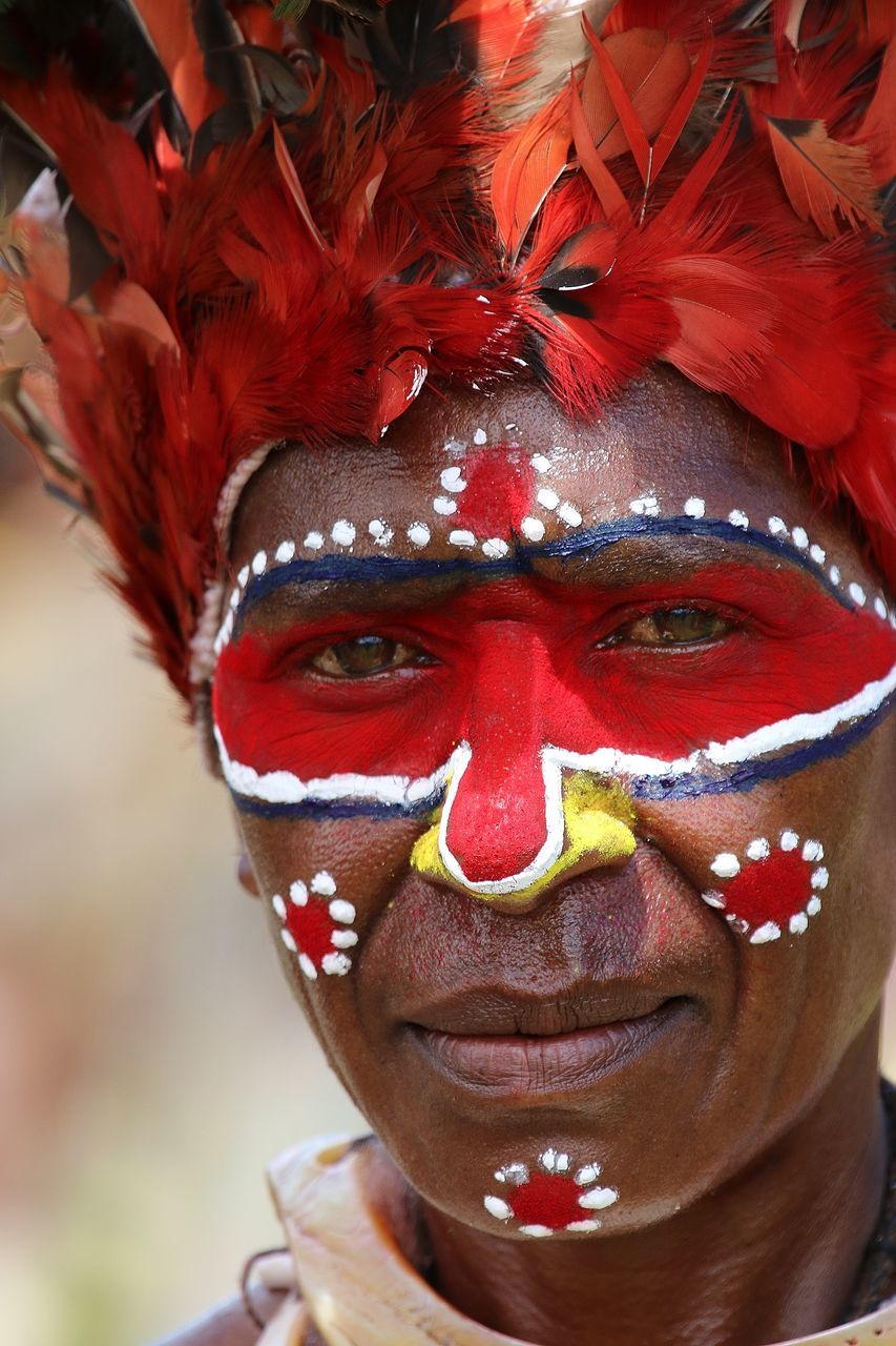 celebration, cultures, tradition, costume, red, real people, front view, one person, traditional festival, headshot, looking at camera, lifestyles, day, face paint, traditional dancing, close-up, venetian mask, headwear, outdoors, portrait, young adult, people