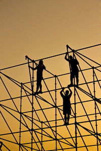 Low angle view of silhouette men working on construction frame against orange sky