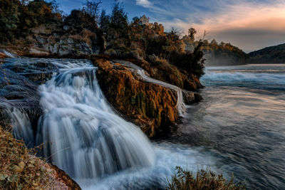 Scenic view of waterfall by sea against sky