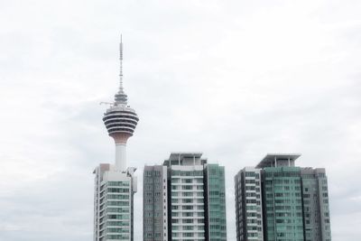 Kuala lumpur tv-tower surrounded by three block of flats. white, cloudy sky.