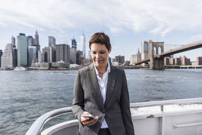 Usa, brooklyn, portrait of businesswoman standing on boat looking at cell phone