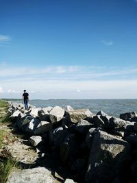 Rear view of man standing on rock by sea against sky