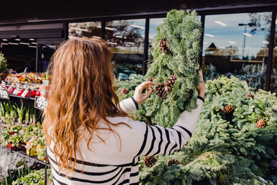 Young woman choosing a decorative green christmas wreath in store or on the market.