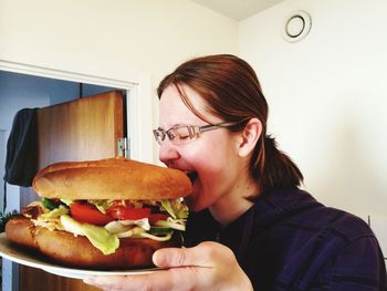 Woman holding plate with hamburger in kitchen at home