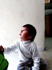Cute boy looking away while sitting on wall