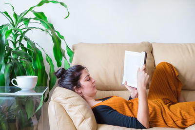 Woman reading book while sitting on sofa at home