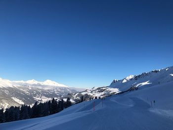 Scenic view of snowcapped mountains and ski piste against blue sky