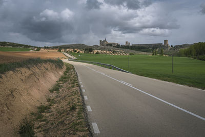 Road amidst fields against a stormy sky with the village of ucles with its famous monastery, cuenca