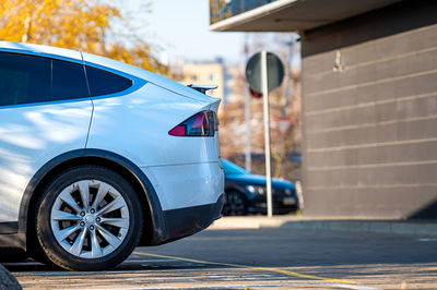 A side fragment of the back of a modern car in a parking lot near an office building on a sunny day