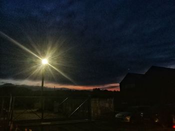 Illuminated street amidst buildings against sky at night