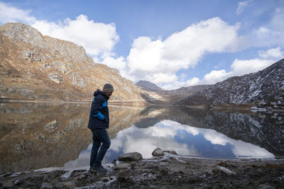 Side view of mature man standing at lakeshore against cloudy sky