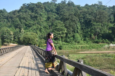 Rear view of woman walking on footbridge against trees