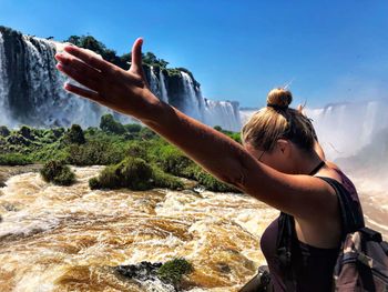 Woman standing with arms outstretched against waterfall