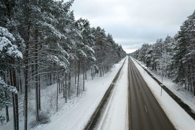 Aerial view of asphalt highway leading through frosty winter forests and groves covered with snow