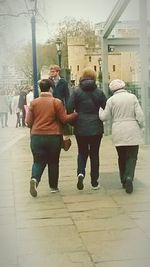 Rear view of people walking on sidewalk in city