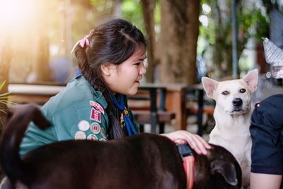 Side view of girl playing with dogs while sitting outdoors